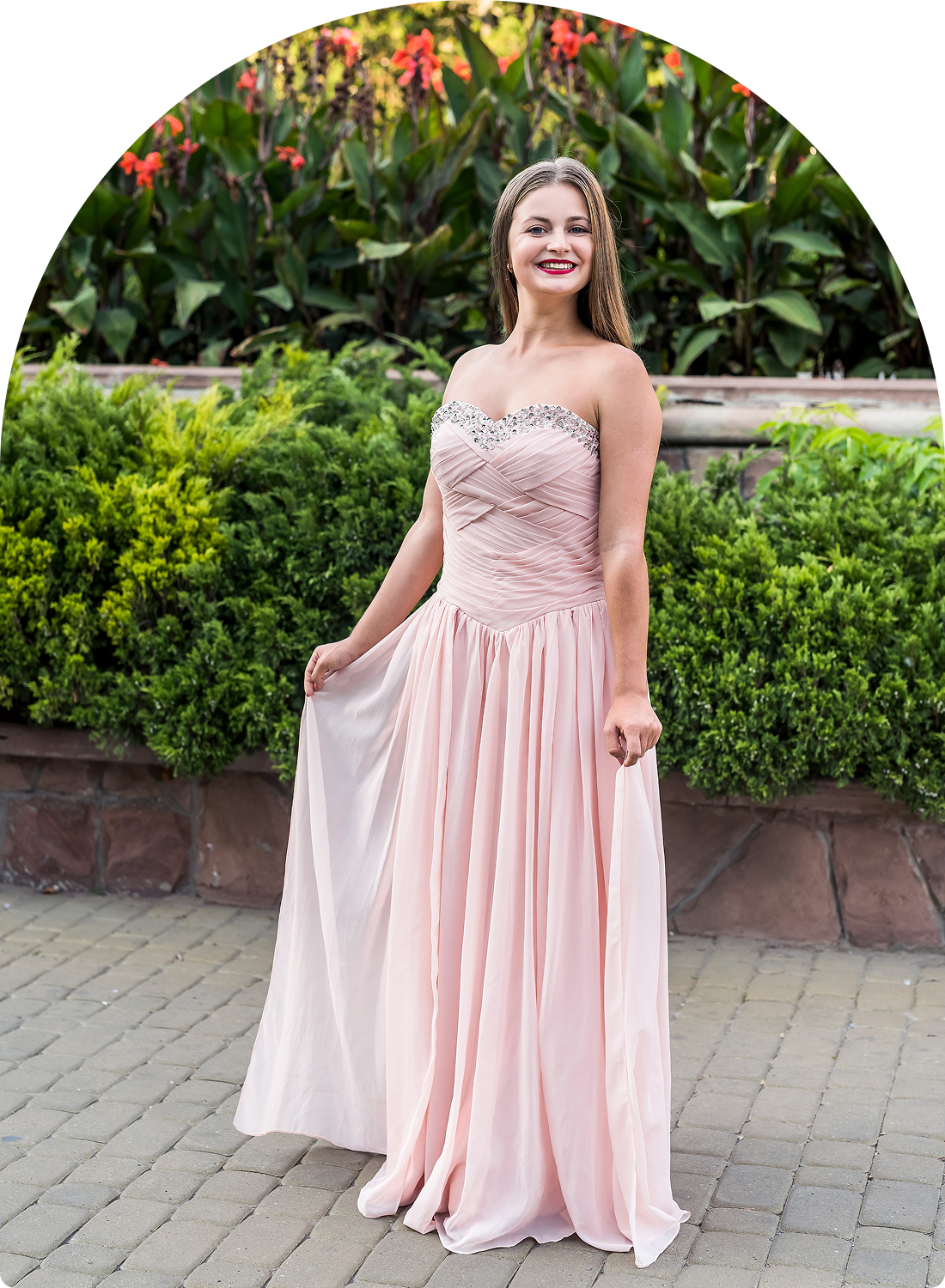 Woman in pink gown smiling outdoors.